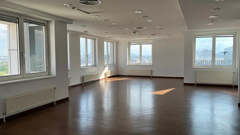 Geräumiger, leerer Büroraum mit vielen Fenstern, Holzboden und natürlichem Lichteinfall.