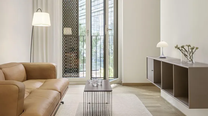 Helles Wohnzimmer mit modernem Sofa, schwebendem Regal und Zugang zu einem französischen Balkon.