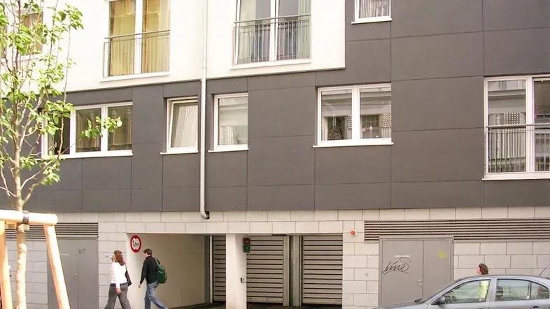 Moderne Fassade eines Wohngebäudes mit grauen Paneelen, weißen Fenstern und Tiefgaragenzufahrt.