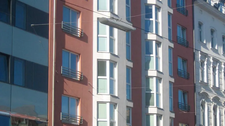 Mehrstöckiges Wohngebäude mit roter und weißer Fassade, vielen Fenstern und kleinen französischen Balkonen in urbaner Umgebung.