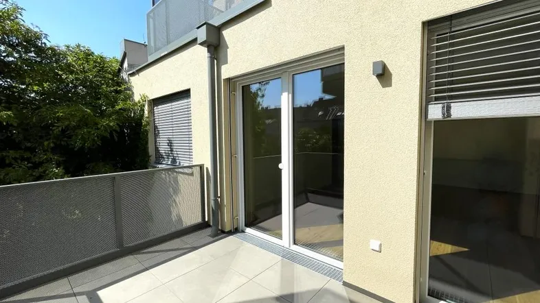 Geräumiger Balkon mit Fliesenboden und Metallgeländer, bietet Zugang zu den Innenräumen und Blick ins Grüne.