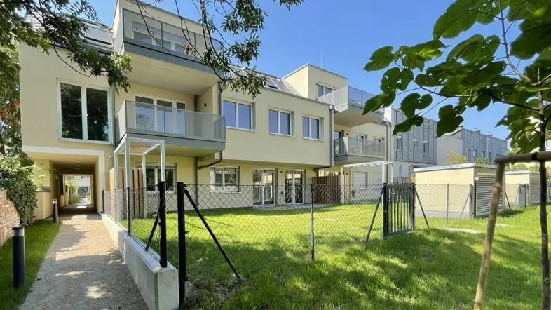 Moderne Wohnanlage mit hellen Fassaden, Balkonen und privaten Gärten im Erdgeschoss.