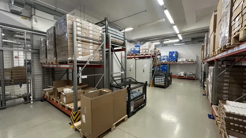 Geräumiger Lagerbereich mit hohen Regalen, Paletten und Kartons, gut beleuchtet für effiziente Logistik.