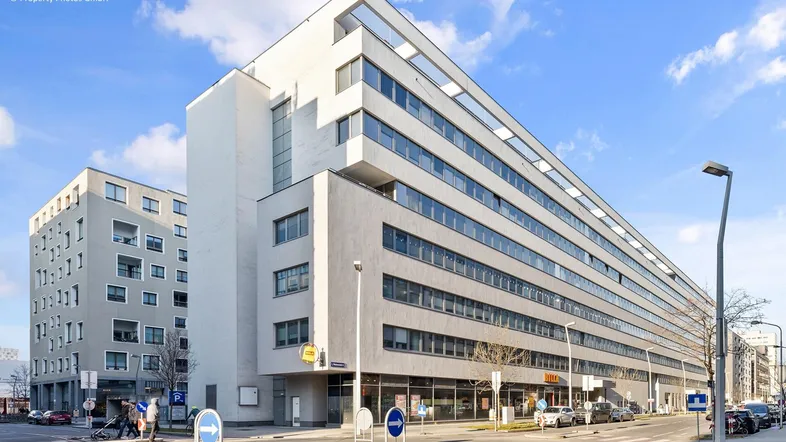 Modernes Geschäftsgebäude mit mehreren Etagen und Ladenflächen im Erdgeschoss an einer belebten Straße.