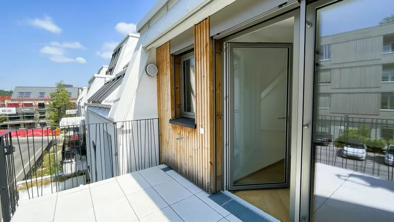 Heller Balkon mit Fliesenboden und Blick auf die umliegenden Gebäude und die grüne Umgebung.