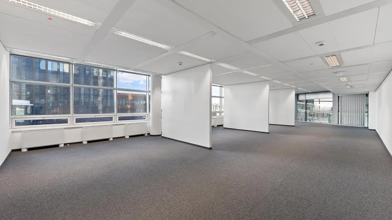 Geräumiges, leeres Büro mit Teppichboden, großen Fenstern und modularen Trennwänden für flexible Nutzung.