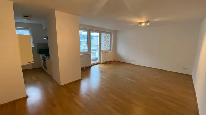 Helles Wohn- und Esszimmer mit Parkettboden und Zugang zum Balkon.