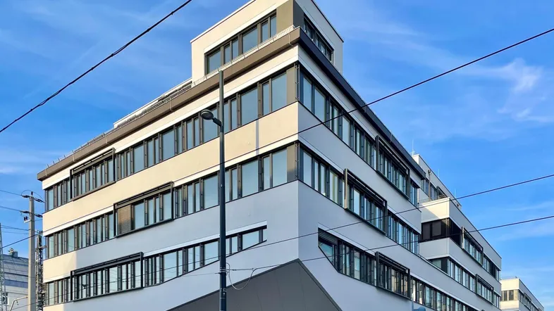 Modernes Bürogebäude mit vielen Fenstern und markanter Architektur unter blauem Himmel.