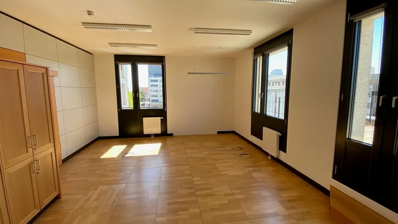 Geräumiger Büroraum mit hellem Parkettboden, großen Fenstern und viel Tageslicht.