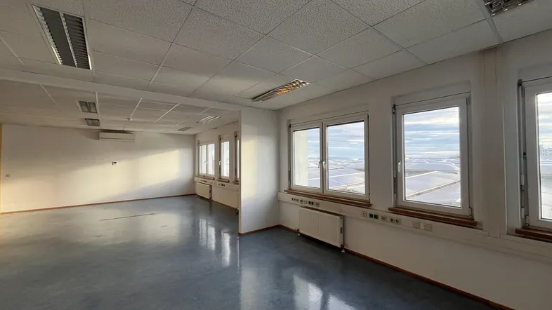 Geräumiges, leeres Büro mit vielen Fenstern, die viel Tageslicht hereinlassen und eine weite Aussicht bieten.