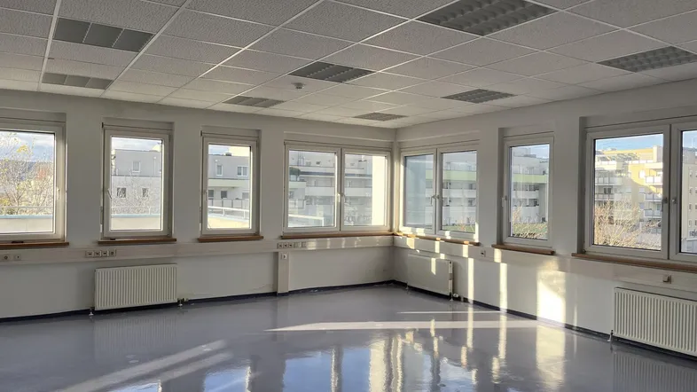 Leerer Büroraum mit vielen Fenstern, die viel Tageslicht hereinlassen und einen Blick nach draußen bieten.