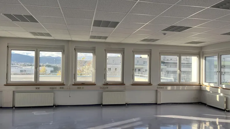 Heller, leerer Büroraum mit vielen Fenstern, die viel Tageslicht hereinlassen und eine weite Aussicht bieten.