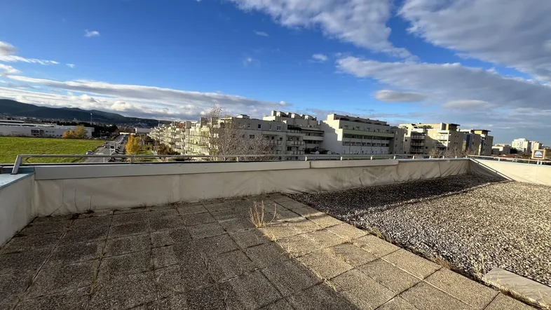 Dachterrasse mit Betonplatten und Kies, bietet einen weiten Blick über die Stadt und die umliegende Landschaft.