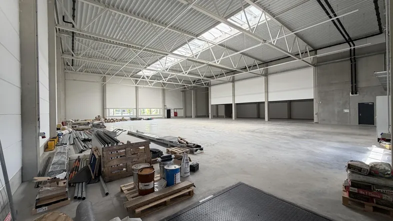 Große, leere Lagerhalle mit Betonboden und hoher Decke, die Tageslicht durch Oberlichter erhält.