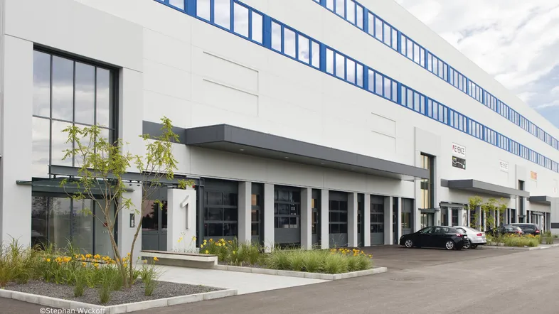 Moderne Geschäftsfassade mit großen Fenstern, mehreren Eingängen und gepflegter Außenanlage, inklusive Parkplätzen.