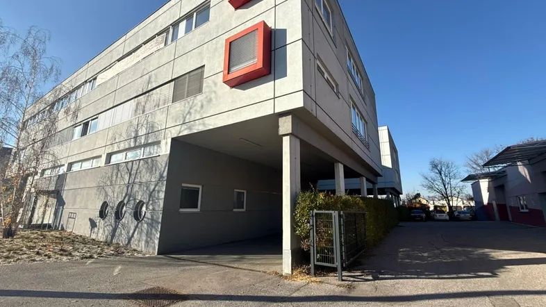 Modernes Bürogebäude mit klaren Linien und roten Akzentfenstern unter blauem Himmel.