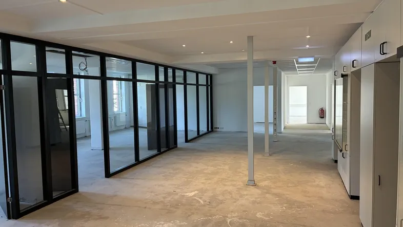 Großer, heller Büroraum mit modernen Glasabtrennungen und Betonboden, bereit für den Ausbau.