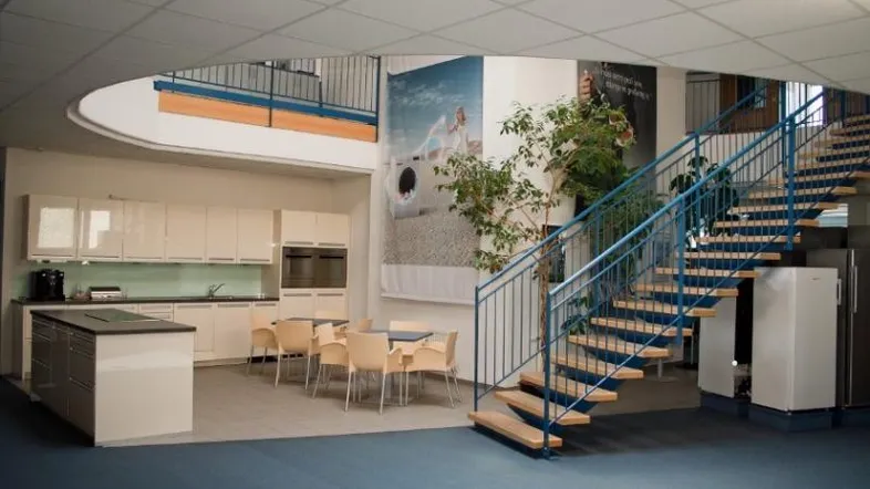 Offener Innenbereich mit Küchenzeile, Esstisch und einer geschwungenen Treppe, die in die obere Etage führt.