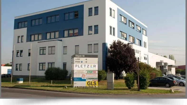 Modernes Bürogebäude mit blauer und weißer Fassade, umgeben von Grünflächen und Parkplätzen.