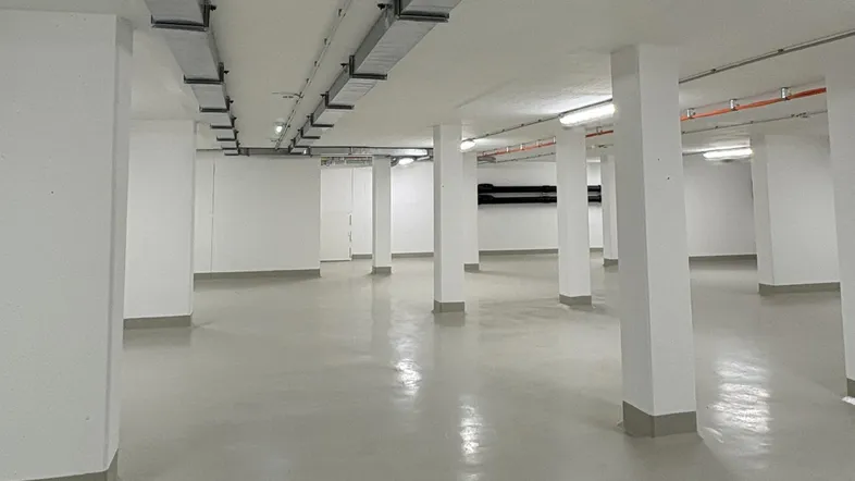 Großer, leerer Raum im Untergeschoss mit vielen Säulen, hellgrauem Boden und sichtbaren Deckeninstallationen.