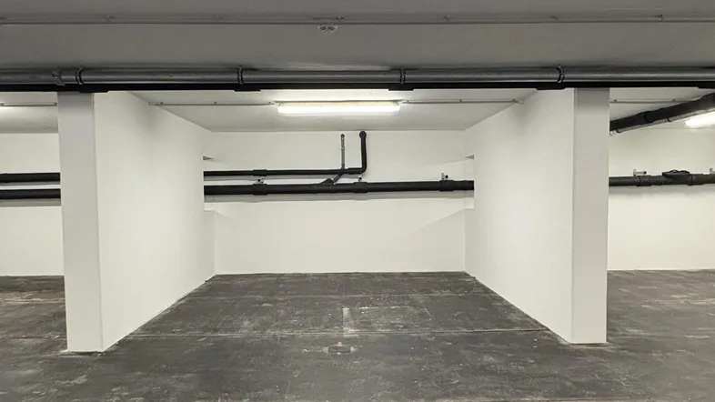 Tiefgaragenstellplatz mit Betonboden und sichtbaren Leitungen an der Decke.