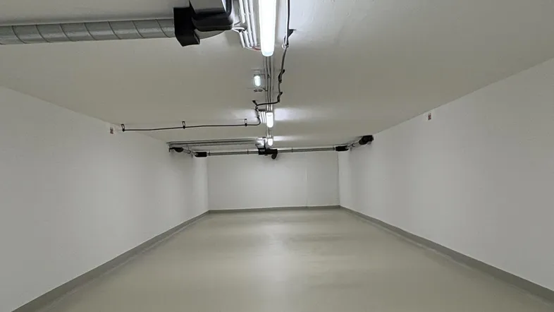 Heller, leerer Raum mit weiß gestrichenen Wänden und sichtbaren Leitungen an der Decke, ideal als Stellplatz.