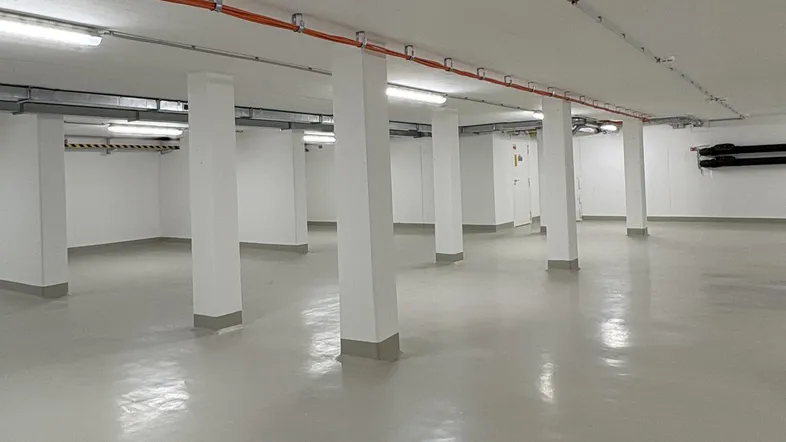 Heller, sauberer Tiefgaragenbereich mit vielen weißen Säulen, glänzendem Boden und sichtbaren Installationen.