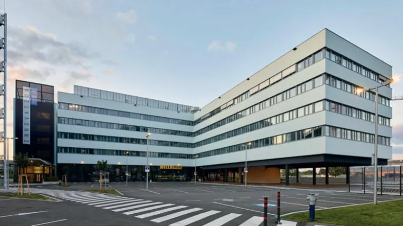 Modernes Bürogebäude mit markanter Architektur und großem Parkplatzbereich unter klarem Himmel.