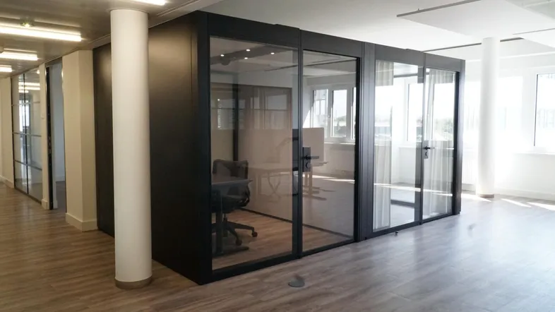 Moderne Büroräume mit Glaswänden und Holzboden, bieten flexible Arbeitsbereiche und viel Tageslicht.
