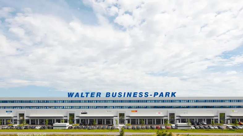 Weitläufiger Walter Business-Park mit moderner Architektur, großem Parkplatz und grüner Umgebung unter blauem Himmel.