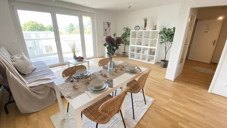 Helles Wohn- und Esszimmer mit Holzboden, modernem Esstisch und Zugang zum Balkon.