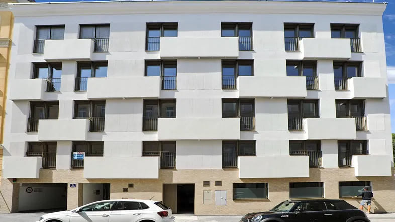 Moderne Fassade eines Mehrfamilienhauses mit weißen Balkonen und dunklen Fenstern.