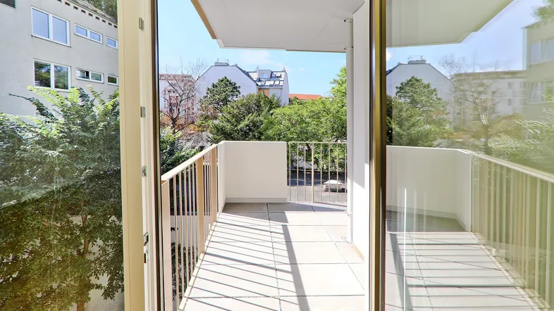 Heller Balkon mit Blick auf grüne Bäume und umliegende Gebäude in städtischer Umgebung.