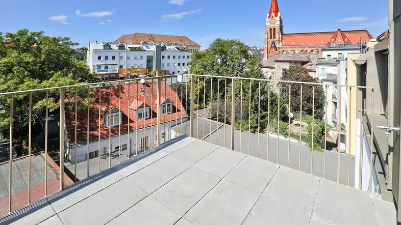 Geräumiger Balkon mit Fliesenboden und weitem Blick über die Stadt und einen Kirchturm.
