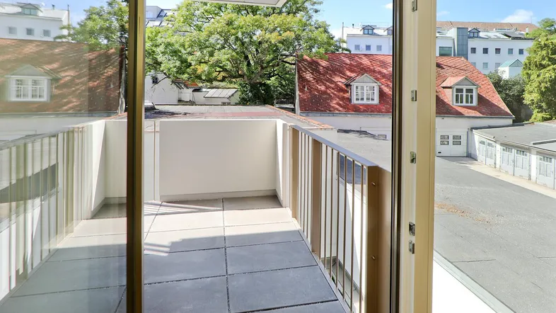 Heller Balkon mit Fliesenboden und Blick auf umliegende Gebäude und Bäume.