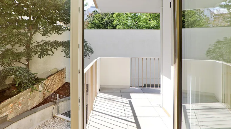 Helle Terrasse mit modernem Geländer und Blick auf den begrünten Innenhof und viel Tageslicht.