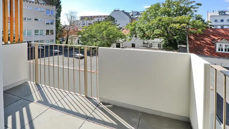 Heller Balkon mit Fliesenboden und Blick auf die umliegenden Gebäude und Bäume.