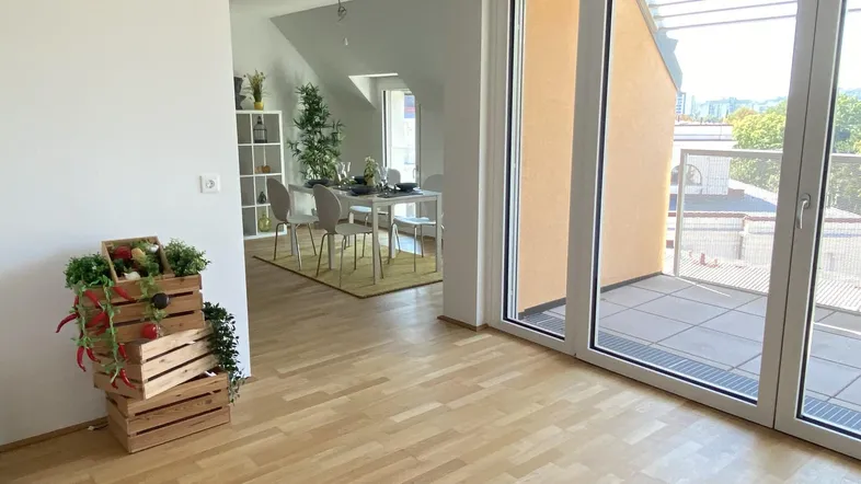 Heller Wohnbereich mit Holzboden, Zugang zur Terrasse und Blick auf den Essbereich im Hintergrund.