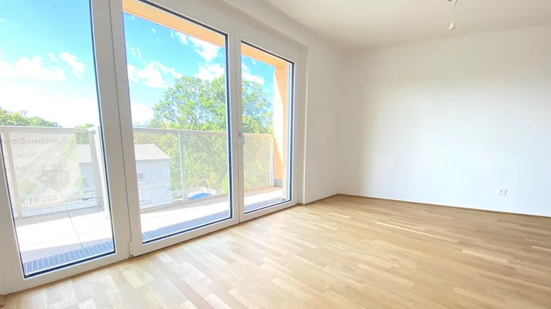 Helles Zimmer mit Holzboden und großen Fenstern, die Zugang zu einem Balkon bieten.