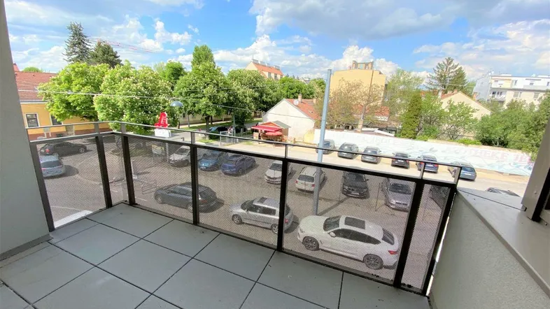Geräumiger Balkon mit Blick auf die Umgebung und einen Parkplatz unter blauem Himmel.