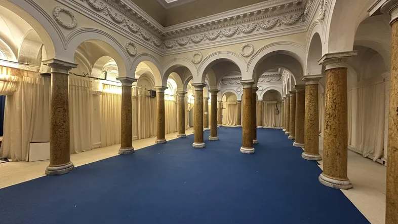 Großer, prunkvoller Saal mit Säulen, Bögen, einem Oberlicht und blauem Teppichboden, ideal für Veranstaltungen.