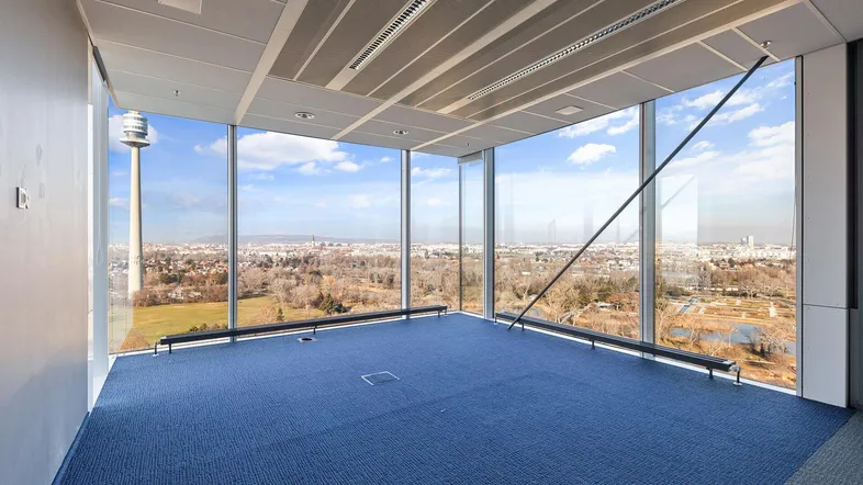 Geräumiges Büro mit blauer Teppichboden und raumhohen Fenstern, die einen weiten Blick über die Stadt bieten.