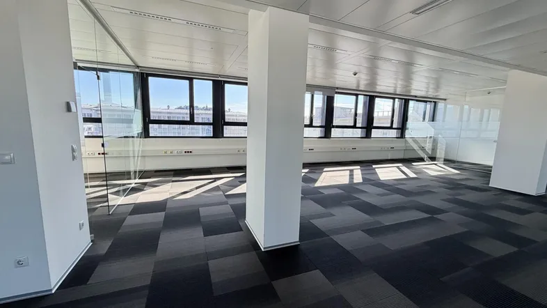 Großes, helles Büro mit Teppichfliesen, Glaswänden und weitem Ausblick durch die Fenster.