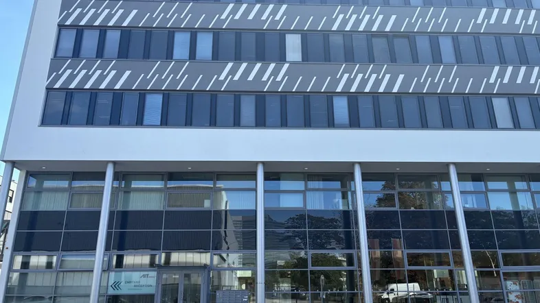 Moderne Bürogebäude-Fassade mit großen Fenstern und weiß-grauer Gestaltung, die eine zeitgemäße Architektur zeigt.