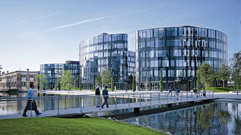 Moderne Bürogebäude mit Glasfassaden und einem Teich im Vordergrund, belebt von Fußgängern.