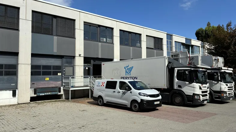 Außenansicht eines modernen Gewerbegebäudes mit mehreren Laderampen und geparkten Lieferfahrzeugen unter blauem Himmel.
