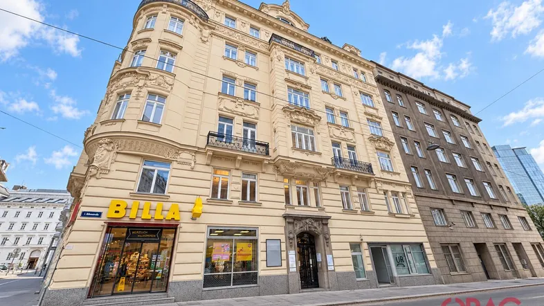 Historisches Gebäude mit klassischer Architektur, Balkonen und einem Supermarkt im Erdgeschoss an einer belebten Straße.