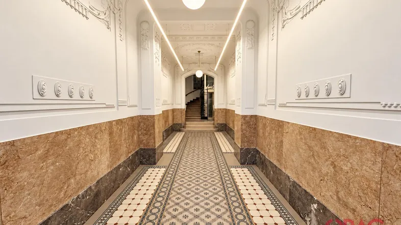 Elegante Eingangshalle mit gemusterten Fliesen, Marmorverkleidung und Stuckverzierungen, die zu einer Treppe führt.