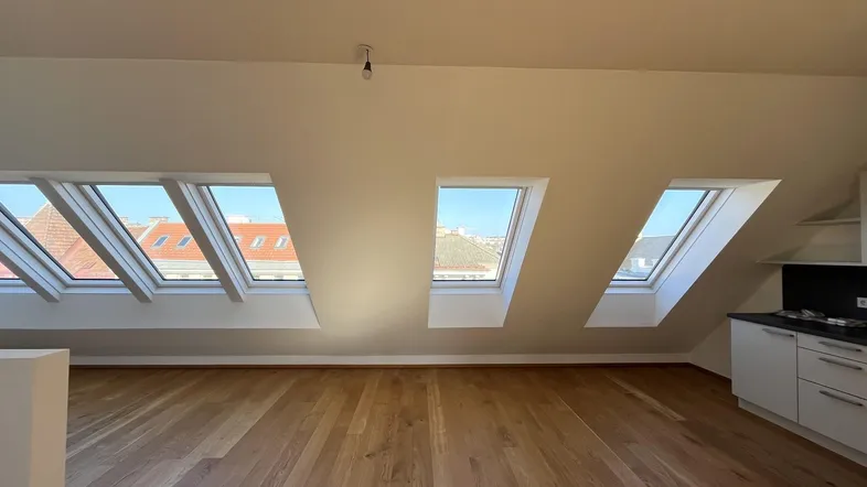 Heller Dachgeschossraum mit mehreren Dachfenstern, Holzboden und integrierter Küchenzeile.