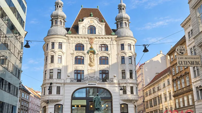 Historisches Gebäude mit reich verzierter Fassade und Türmchen an einer belebten Straßenecke in der Stadt.